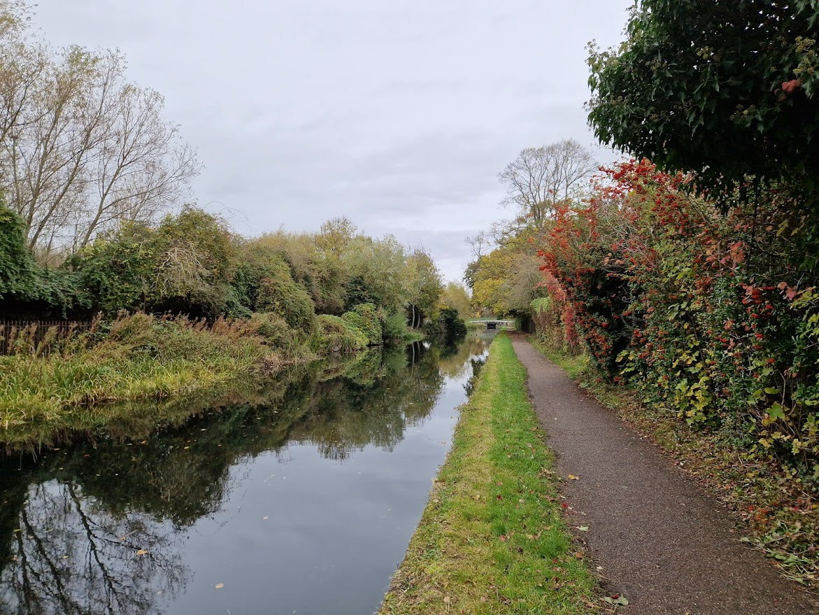 Narrow canal with a path on either side, surrounded by trees and greenery.